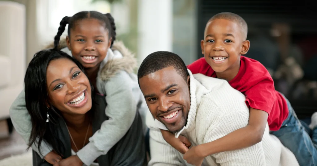 Happy family of four smiling inside their home with a backup generator providing storm power protection.