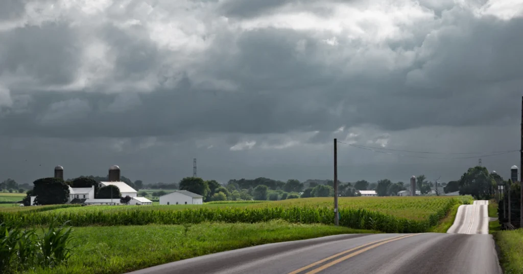 Rural Western PA farm along a country road with dark spring storm clouds approaching in the distance.