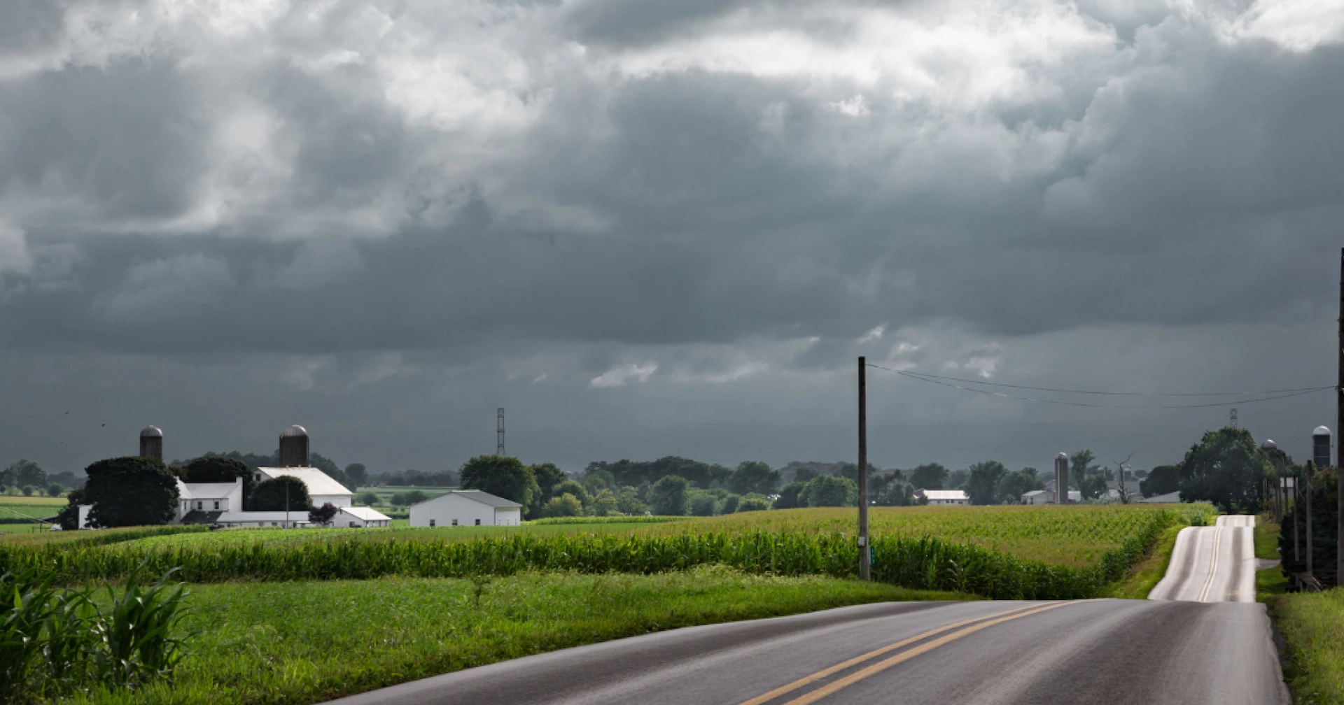 Rural Western PA farm along a country road with dark spring storm clouds approaching in the distance.
