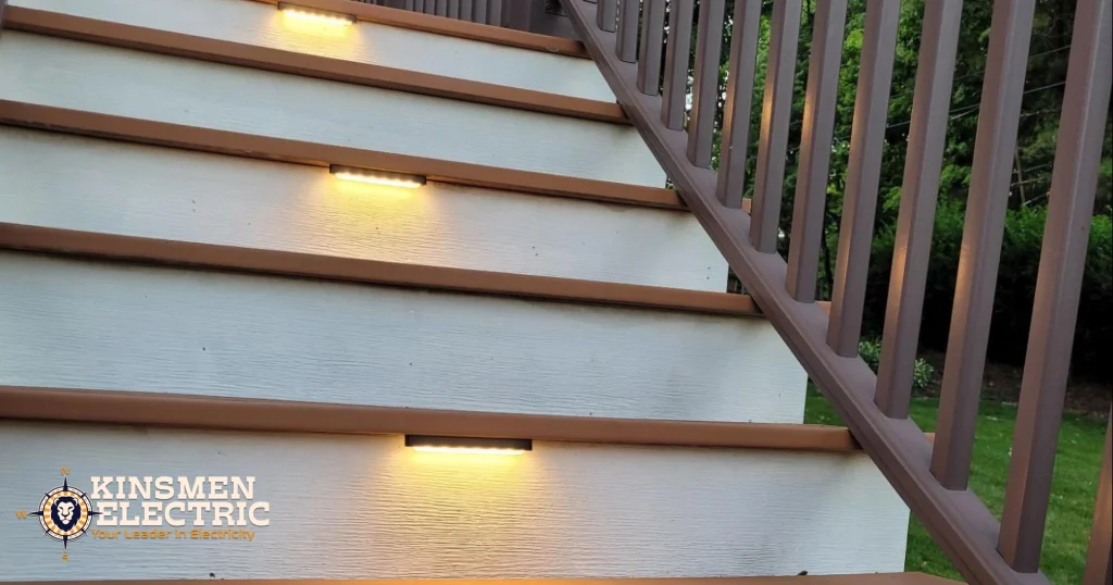 Composite deck stairs with built-in LED step lights glowing at dusk, featuring brown treads, white risers, and a dark railing.