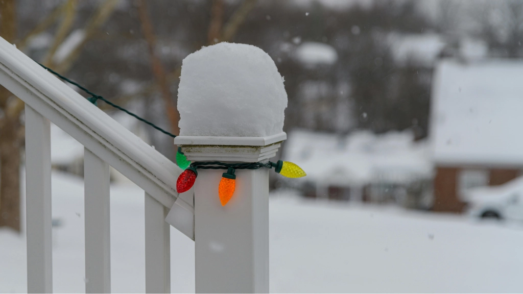 a string of Christmas lights is wrapped around a snow-capped outdoor railing