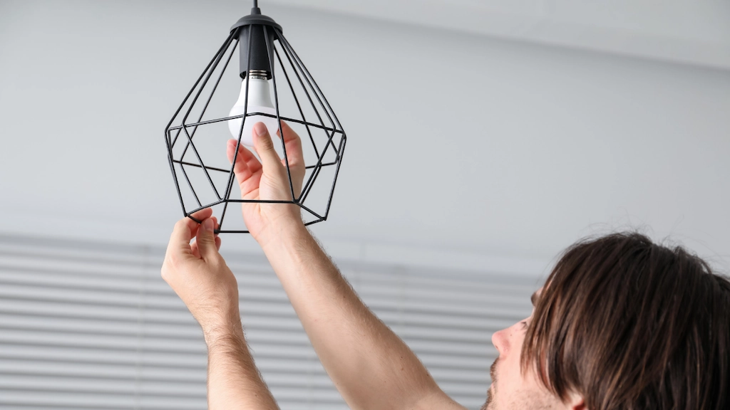 man installing a lightbulb into a light fixture in a home